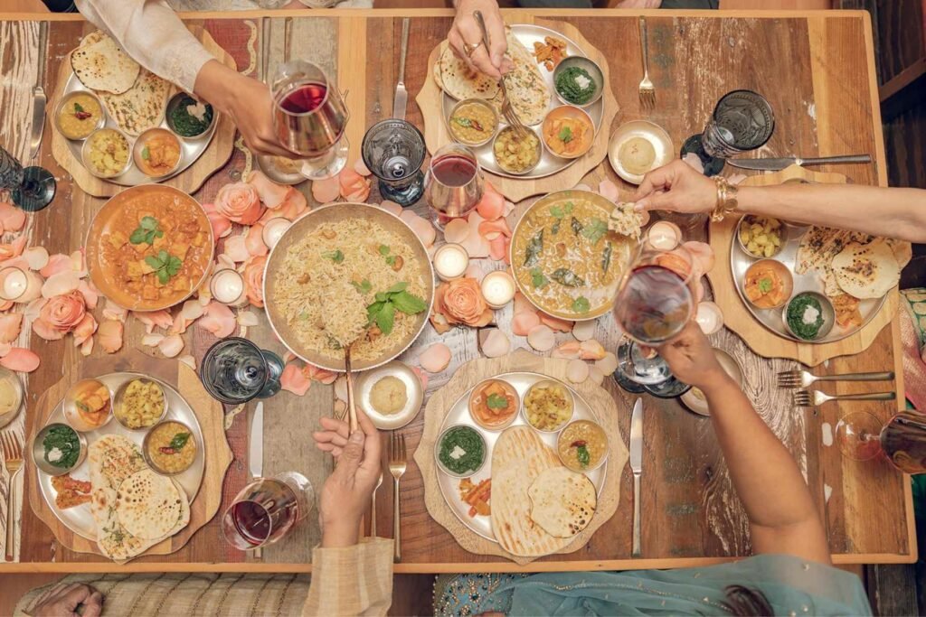Dishes served at a shared meal: saag, paneer masala, jeera aloo, yellow dal tadka, navratan korma, achar, naan bread, veg biryani, papad, sheera, gulab jamun, rasgulla.